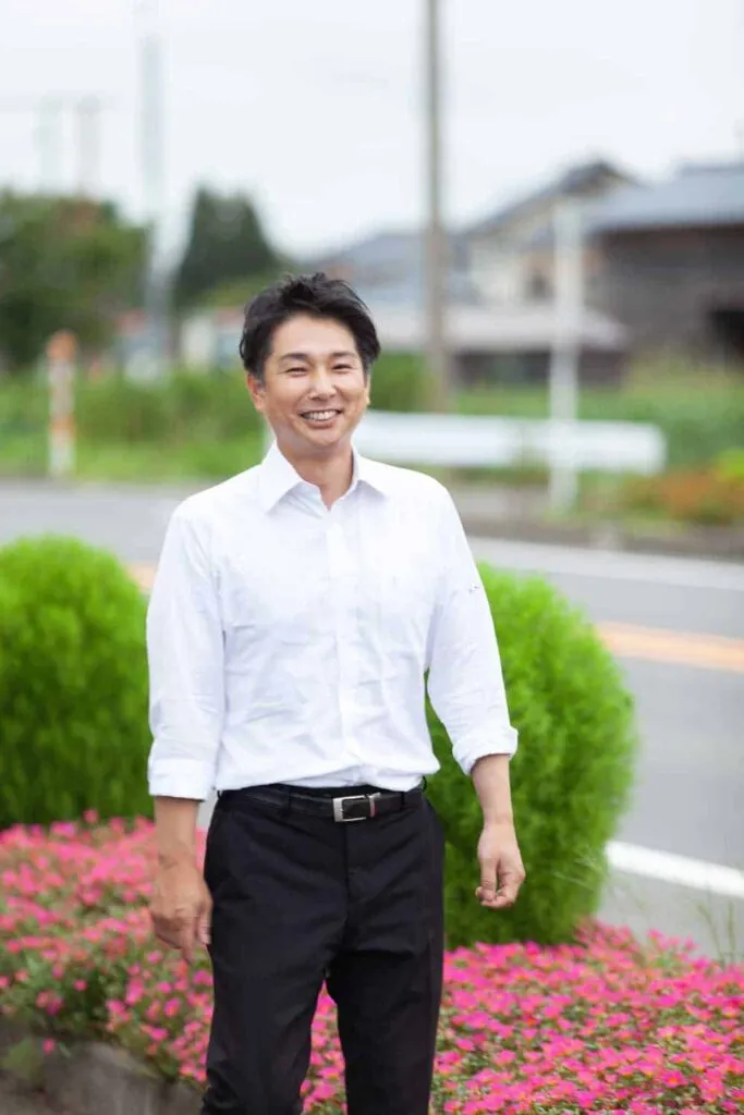 笑顔の男性。プロフィール写真。屋外で花と緑を背景に立つ。